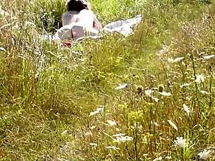 A young guy is spying on a naked MILF sunbathing in public